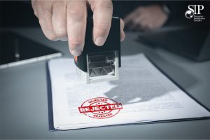 Close-up of a hand stamping a document with a red “REJECTED” mark in an office setting.